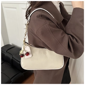 Détail du sac à bandoulière en cuir blanc cassé avec breloque cerise sur manteau brun