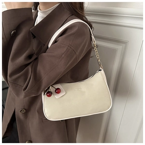 Détail du sac demi-lune crème avec pendentif cerise et bandoulière en chaîne dorée