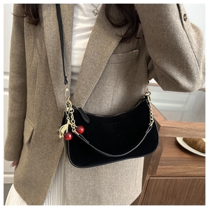 Détail du sac croissant en daim noir avec chaîne dorée et pendentif cerise