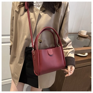 Detail of burgundy leather bucket bag with dual handles and slim crossbody strap