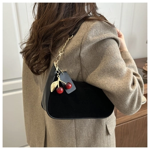 Détail du sac hobo noir en demi-lune avec chaîne dorée et accessoire cerise rouge