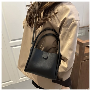 Detail of a minimalist black leather bucket bag worn as a shoulder bag in a stylish room