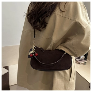 Détail du sac croissant en daim marron foncé avec un pendentif décoratif cerise rouge