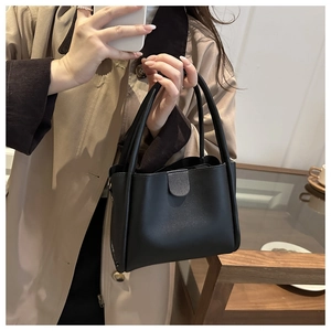 Detailansicht einer schwarzen Lederhandtasche mit runden Griffen auf einem Trenchcoat