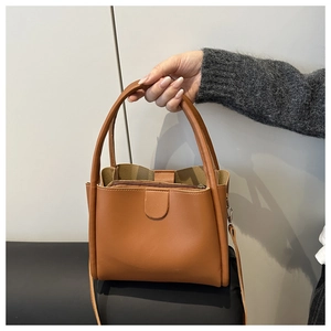 Detail of a brown leather bucket bag with three compartments and adjustable shoulder strap