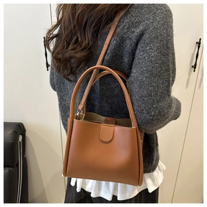 Sac seau en cuir marron porté avec un pull gris et une jupe blanche pour un look d'automne