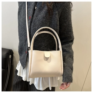 Detail of a creamy white leather handbag shown with crossbody strap and top handle