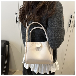 Detailed view of a creamy white minimalist bucket bag with twin handles and magnetic closure