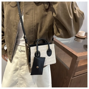 Detail of woven straw small square bag with black leather straps and hanging mini pouch