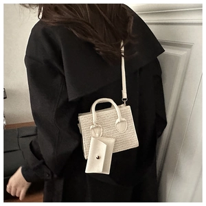 Detail of cream woven mini handbag and matching small envelope pouch on a model's coat