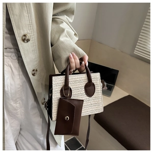 Close-up of cream woven handbag featuring brown leather handles and small charm bag