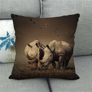 Linen pillowcase detail showing rhinos and birds in a wildlife landscape print on a grey sofa