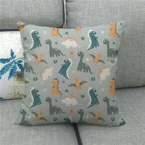 Detail of linen cushion cover featuring colorful cartoon dinosaurs on a gray sofa