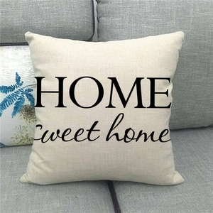 Beige linen cushion cover with black HOME Sweet home print on a gray fabric sofa