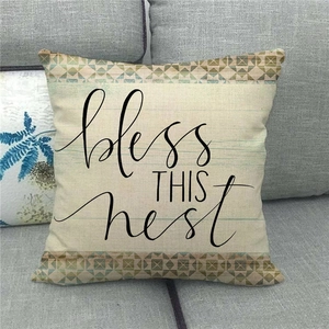 Detail of linen pillowcase featuring black bless THIS nest text on a gray sofa