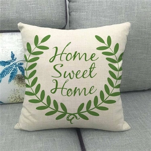 Close-up of linen pillow cover with Home Sweet Home text and olive wreath on a sofa