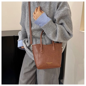 Détail d'un sac bandoulière en cuir marron avec poignées porté par un mannequin