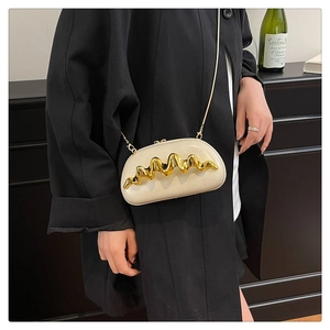 Detail of cream shoulder bag featuring wavy gold hardware and a metallic chain strap