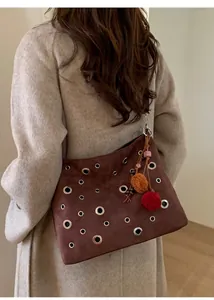 Close-up of brown suede tote bag featuring silver metal grommets and colorful pom-poms