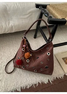 Close-up of brown suede hobo bag featuring silver eyelets and a colorful pompom charm