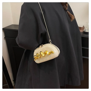 Detail of a creamy white crossbody box bag with wavy gold hardware on a black coat