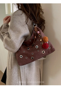 Close-up of brown suede shoulder bag featuring decorative metal grommets and colorful charms