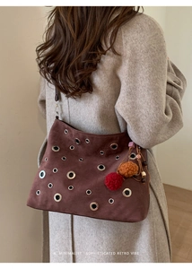 Close-up of brown suede bag featuring silver grommets and colorful tassels on the side