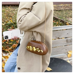 Close-up of a retro brown leather handbag with a gold wave-pattern metal clasp and chain