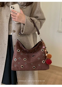 Detail of dark brown suede shoulder bag with silver eyelets and ethnic charm accessory