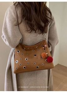 Close-up of brown suede bag with metal eyelets and colorful pom-pom charm on grey coat