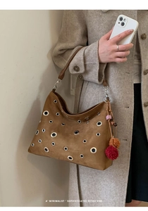 Detail view of brown suede shoulder bag featuring large silver metal eyelets and plush charm