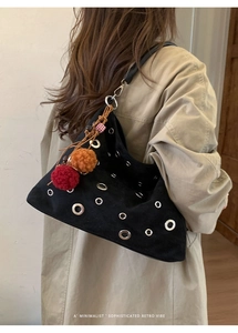 Detail of retro black suede shoulder bag with silver eyelets and colorful plush charms