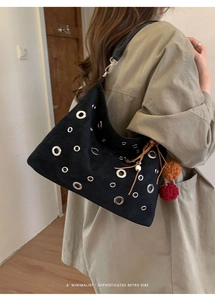 Detail of black suede tote bag with silver metal eyelets and colorful plush charms