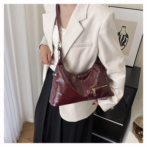 Detail of burgundy patent leather hobo bag with gold zipper and adjustable shoulder strap