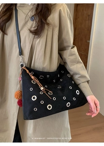 Detail of black suede tote bag with silver eyelets and colorful tassel charm on coat
