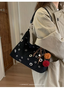 Detail of black suede shoulder bag with metal eyelets and decorative colorful fur balls