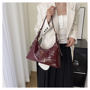 Détail du sac hobo vernis bordeaux avec finitions dorées porté par un mannequin