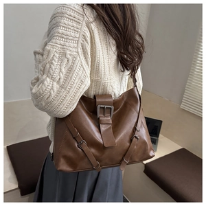 Detail of dark brown leather tote bag showing metal buckle and retro strap accents