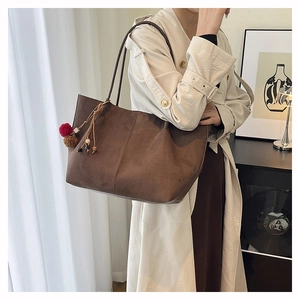 Detail of a large brown suede tote bag featuring a decorative pom-pom and wooden bead charm