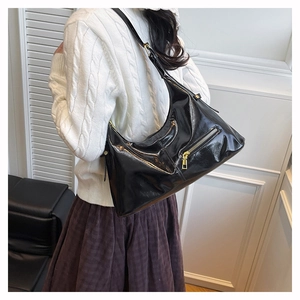 Sac hobo noir brillant avec fermeture éclair dorée porté par un mannequin en intérieur