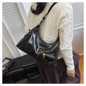 Detail einer glänzenden schwarzen Lackledertasche mit goldenen Beschlägen auf weißem Pullover