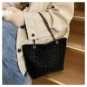 Close-up of leopard print tote bag with metal chain strap worn on a beige trench coat