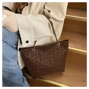 Detail of leopard print tote bag with gold chain strap on a model wearing a beige coat