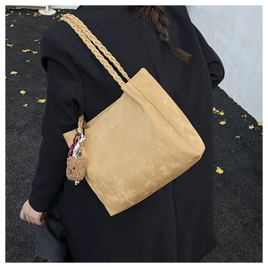 Detail of ginger suede tote bag with braided handle and plush bear charm on black coat