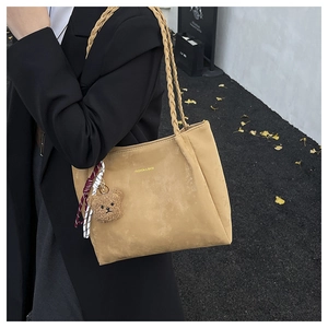 Detail of light brown matte tote bag with woven straps and cute plush bear charm