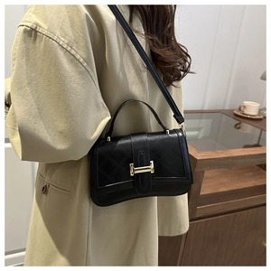 Sac à main matelassé noir avec boucle dorée porté par un mannequin en manteau beige