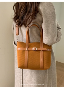 Close-up of yellow woven tote bag with silver buckle worn over a beige wool coat