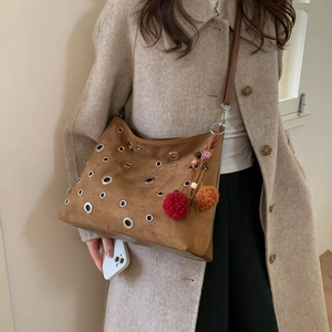 Brown suede shoulder bag with silver eyelets and plush pom-poms on a trench coat model