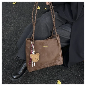 Detail of dark brown tote bag with woven straps and cute teddy bear charm accessory