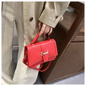 Détail du sac bandoulière rouge matelassé avec boucle H dorée sur manteau beige chic